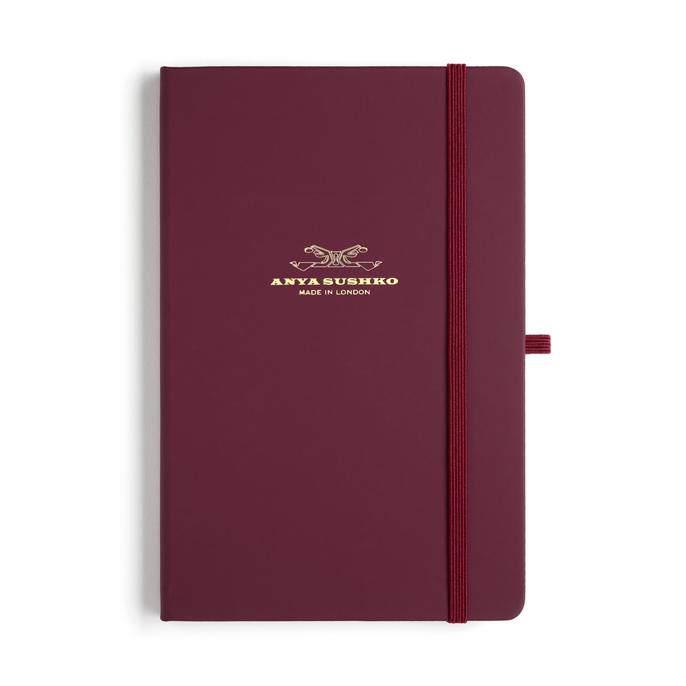 A burgundy A5 hardback refill Luxury notepad with a gold embossed brand logo at the front and a matching elastic pen holder.