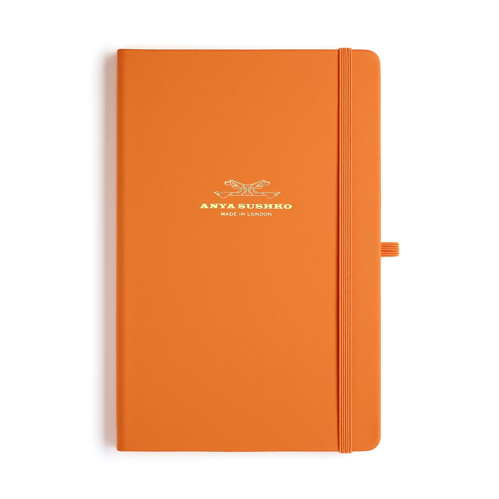 An orange hardback A5 refill Luxury notepad with a ribbon bookmark and elastic pen holder, featuring the Anya Sushko brand logo embossed in gold at the front.